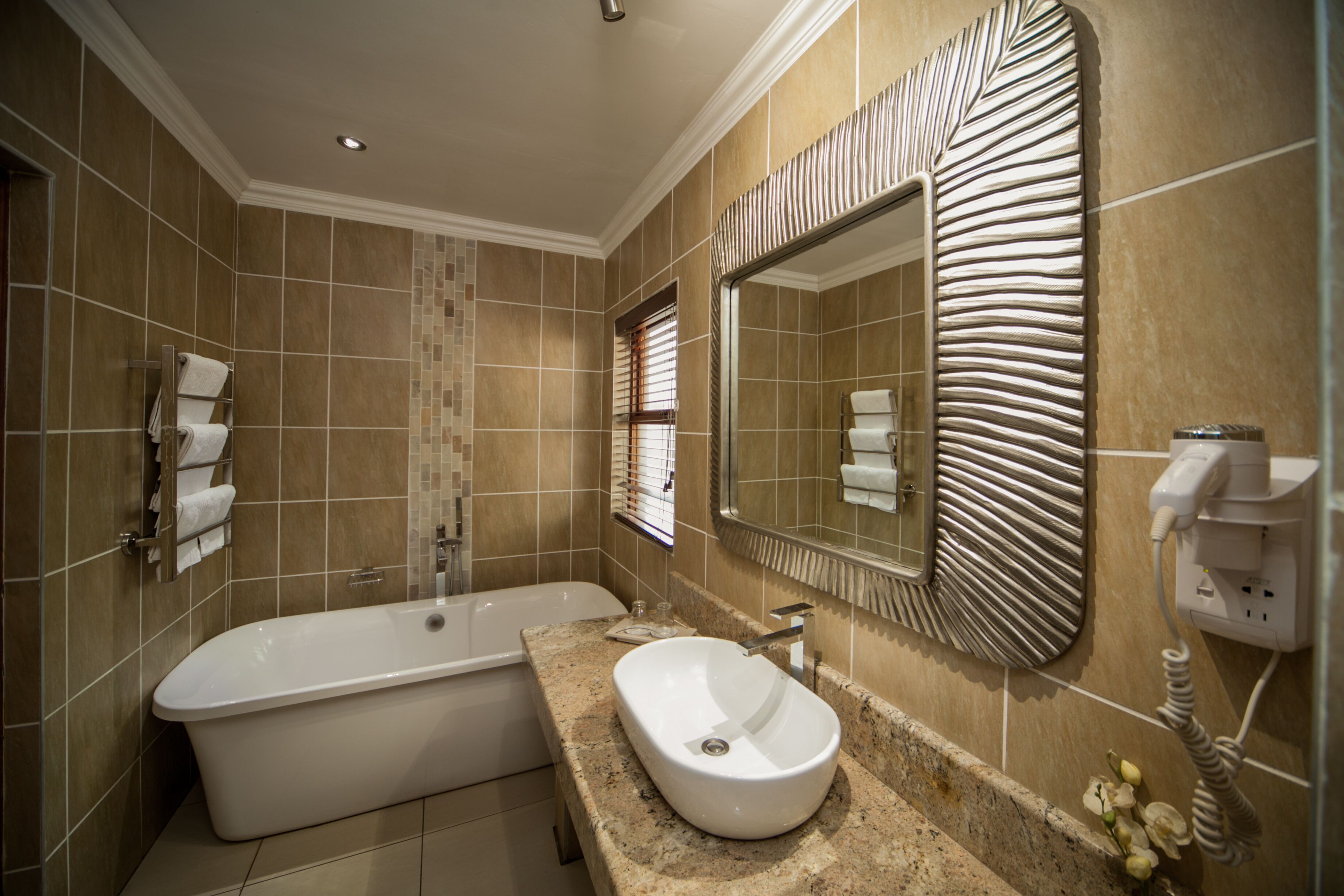 Un baño moderno con una bañera independiente, un lavabo con recipiente y un espejo grande de diseño original.