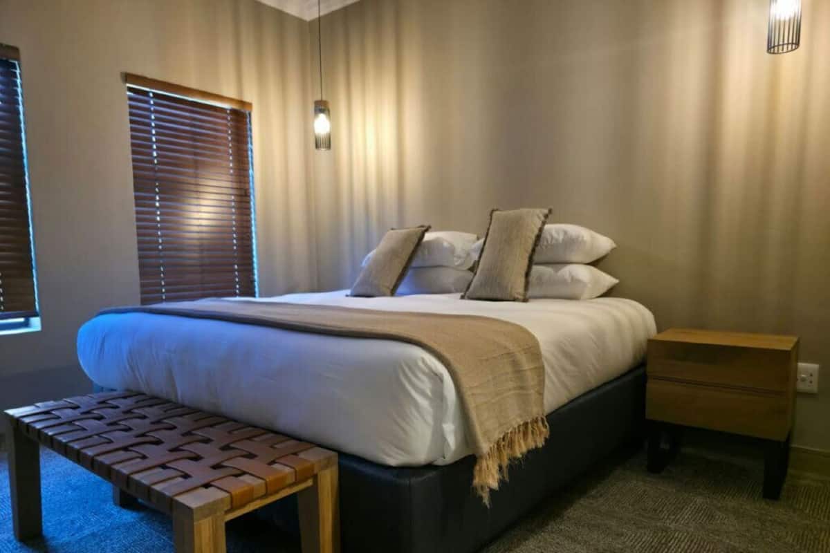 A bedroom with a bed, bedside tables, a bench, and a window with blinds.