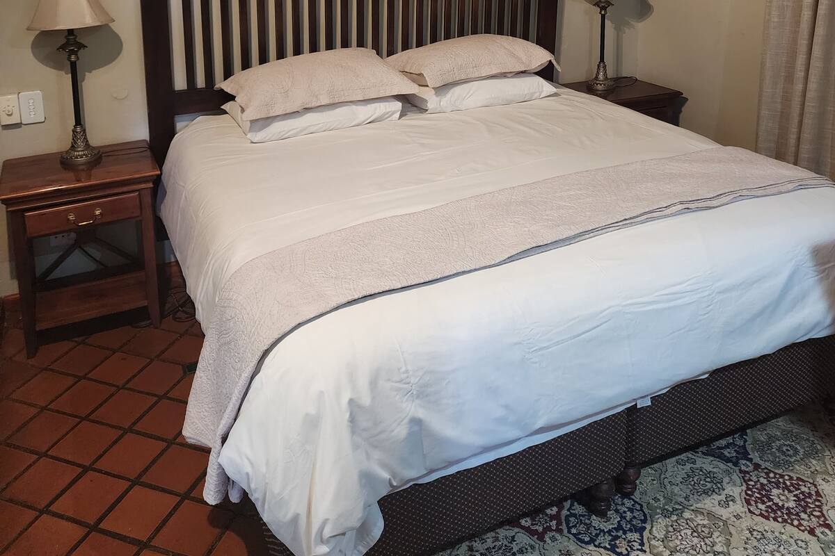 A neatly made bed with a wooden headboard, two bedside tables with lamps, and two framed pictures on the wall.