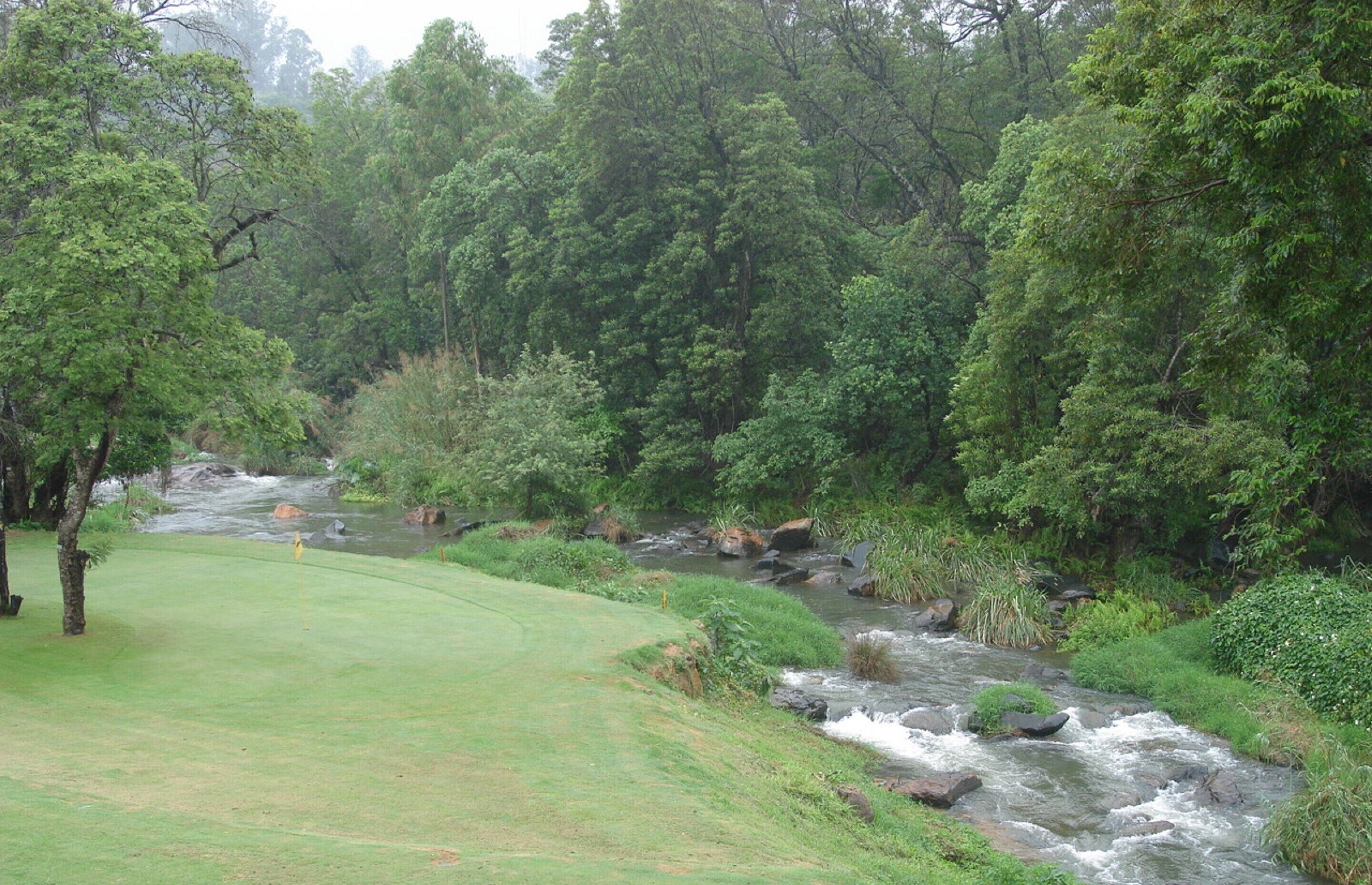 A golf course with a river running through it, surrounded by dense trees.