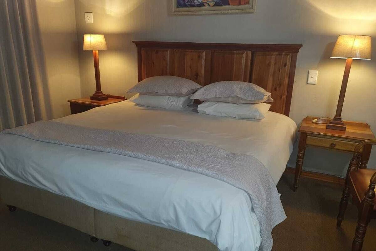 A neatly made bed with a wooden headboard, two bedside lamps, and a small wooden nightstand with a lamp.
