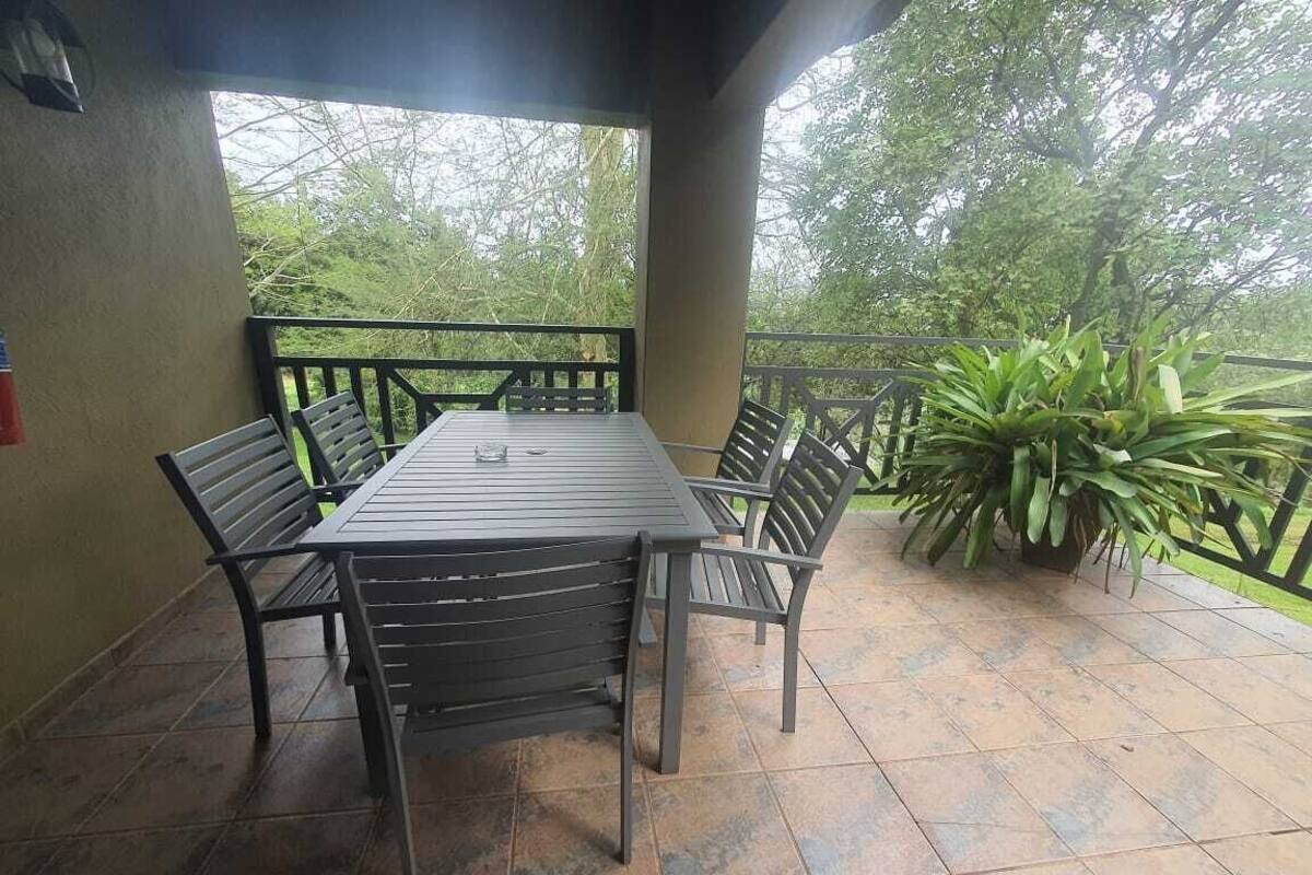 An outdoor patio with a rectangular table and six chairs, surrounded by a tiled floor and a railing.