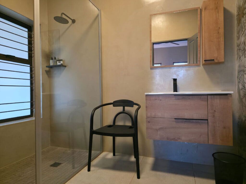 Een badkamer met een douche, een stoel, een houten wastafel en een spiegel.