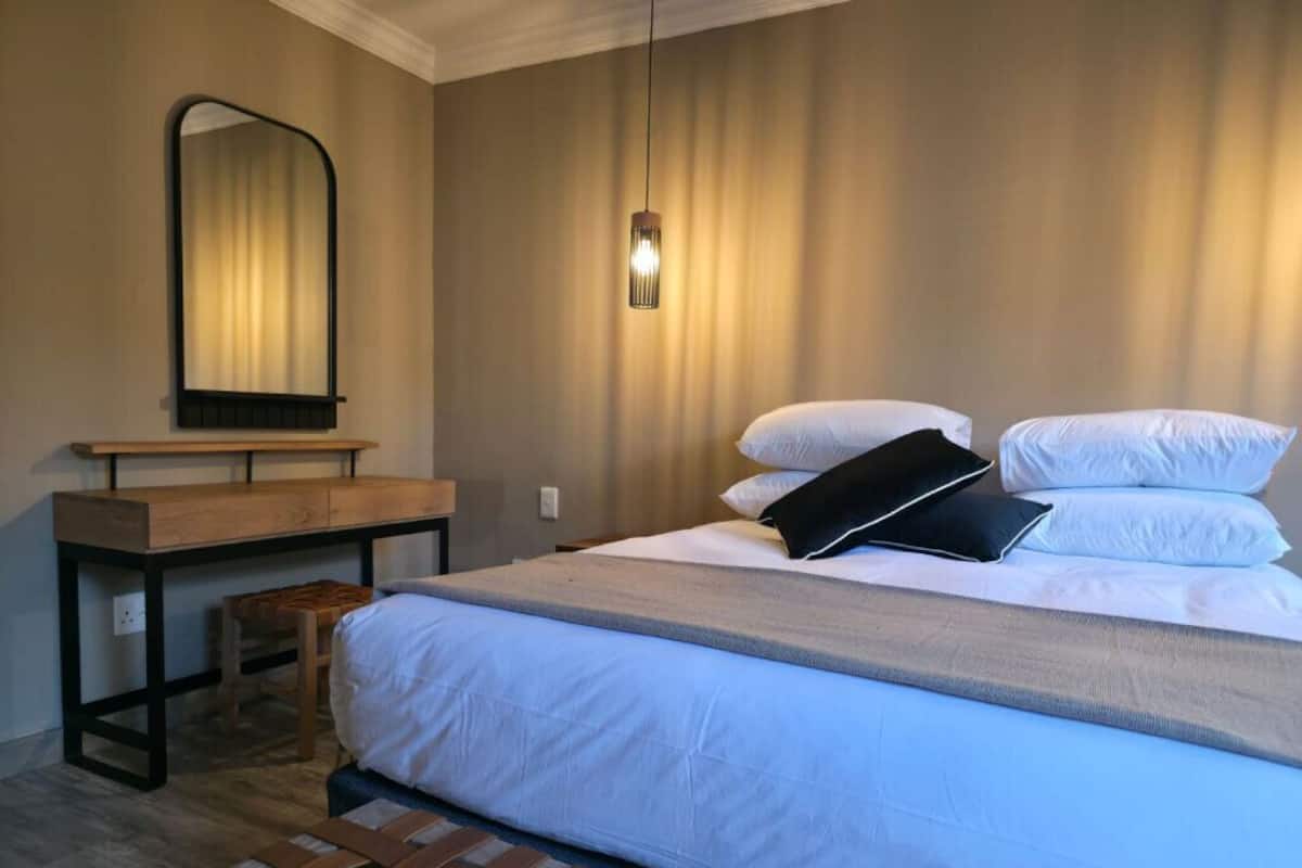 A bedroom with a bed, a wooden bench, a mirror, and a wall-mounted light fixture.