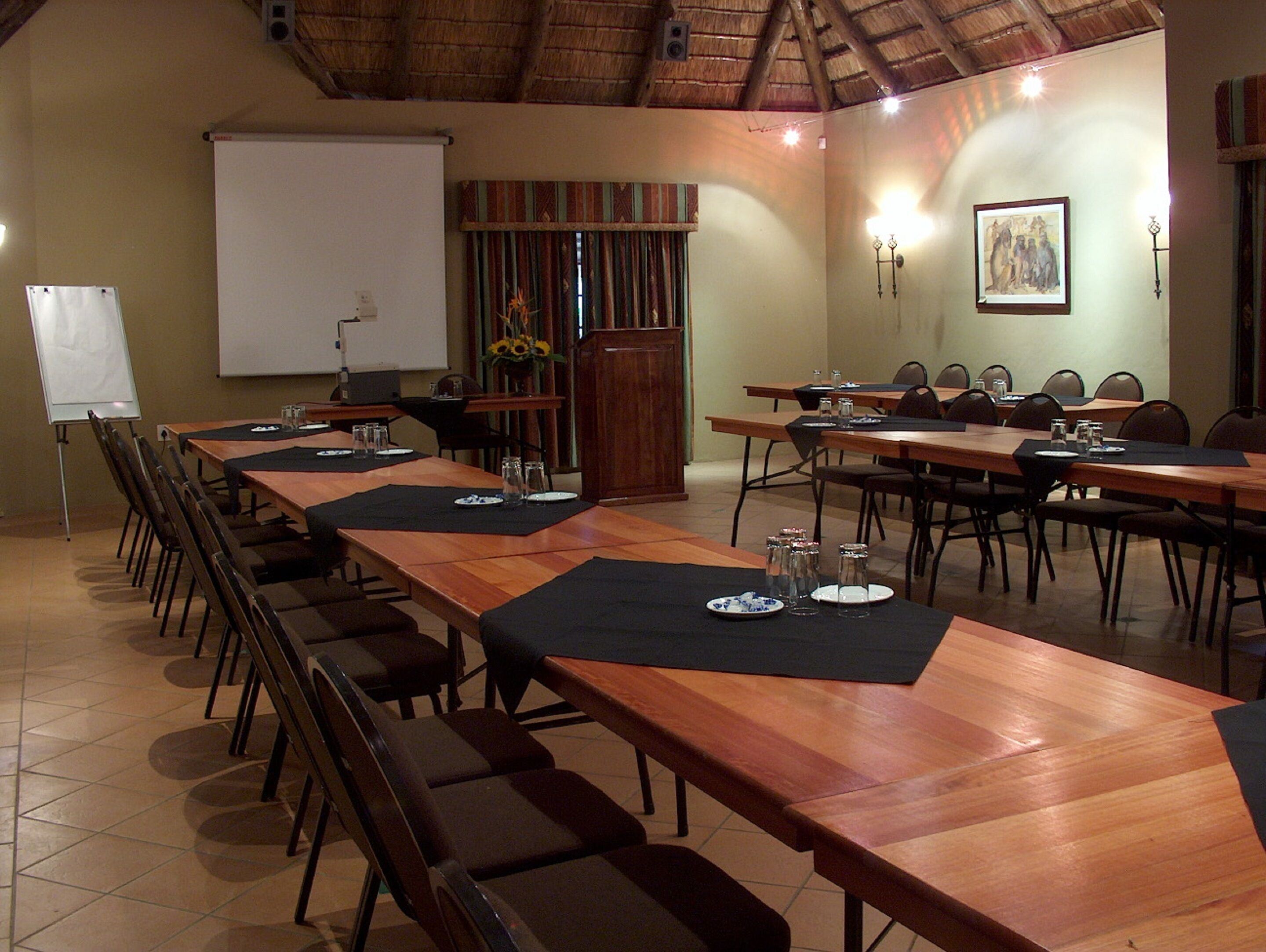 A conference room with long tables, chairs, a whiteboard, and a projector.