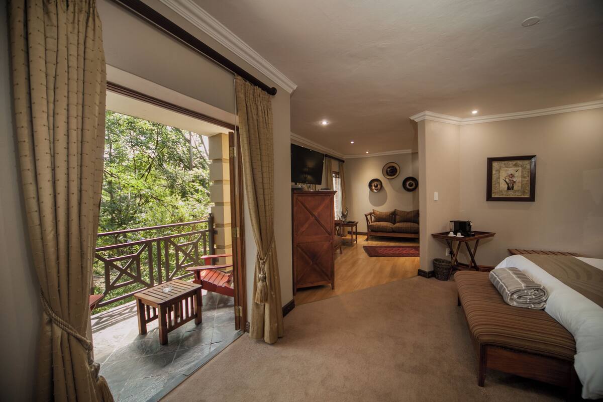 A hotel room with a balcony, a bed, a sofa, and a dining area.