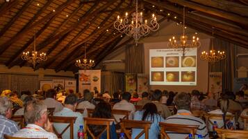 Un salón de conferencias con mesas y sillas de madera, candelabros y una pantalla para presentaciones.