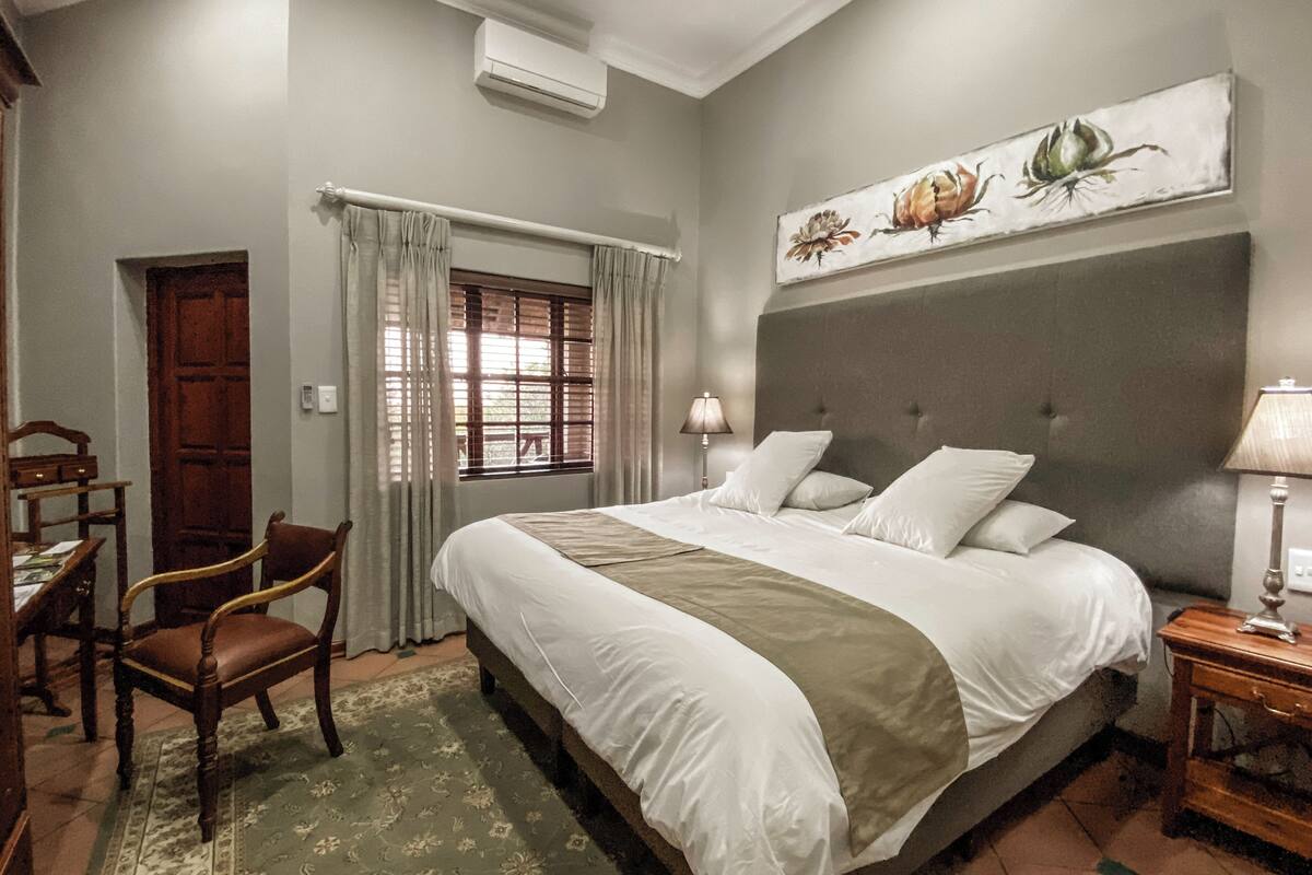 A bedroom with a large bed, a wooden chair, a desk, and a painting on the wall.