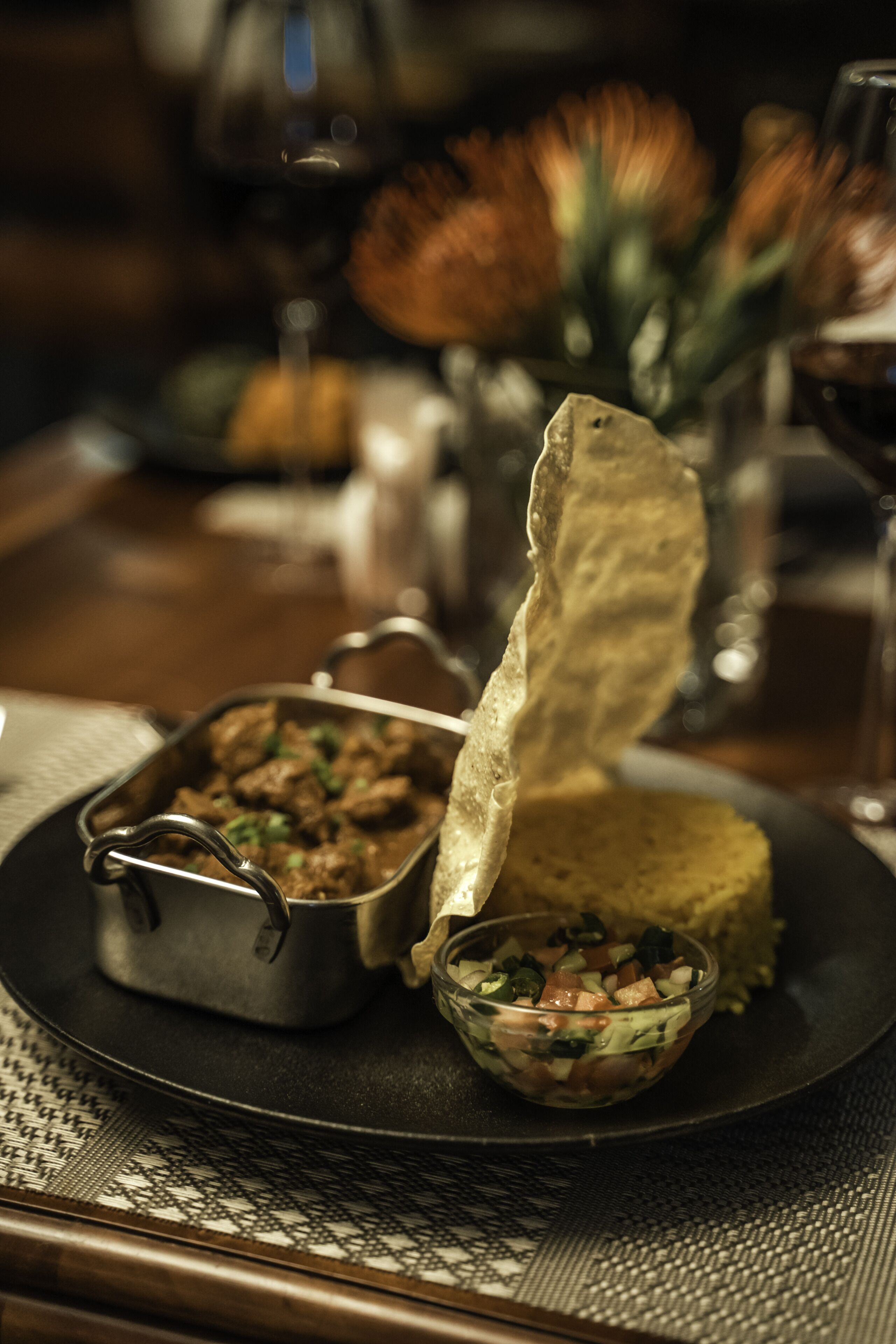A dining table with a metal serving dish containing a meat dish, a bowl of salad, and a folded tortilla.