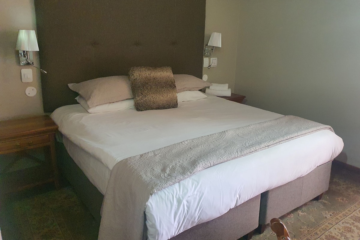 A neatly made bed with a headboard, two bedside lamps, and a bedside table with a lamp.