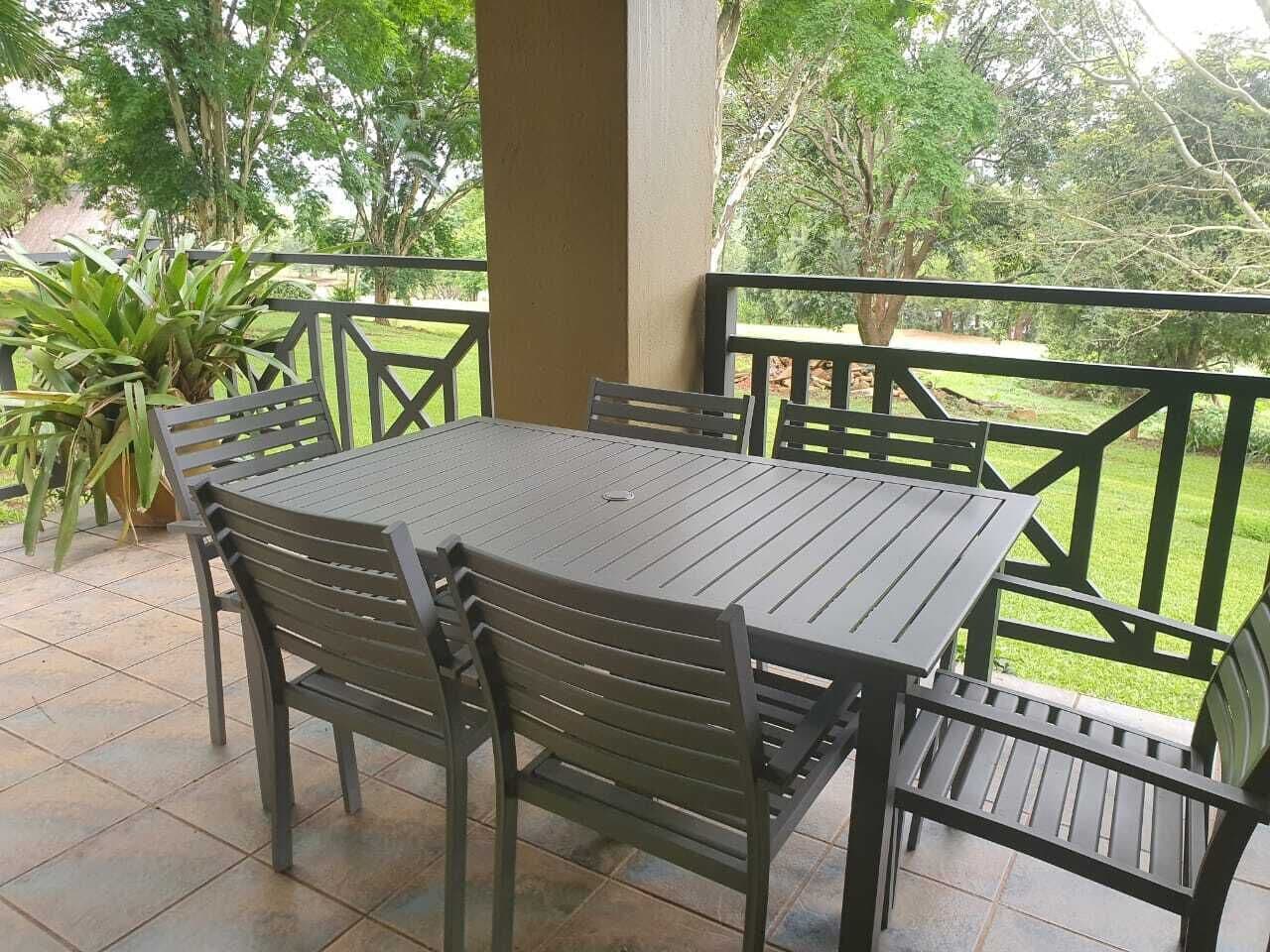 An outdoor patio with a round table and chairs, surrounded by a railing with a view of greenery.