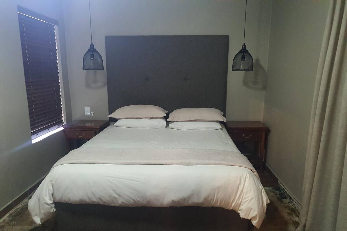 A neatly made bed with a headboard, two bedside tables, and a window with blinds.
