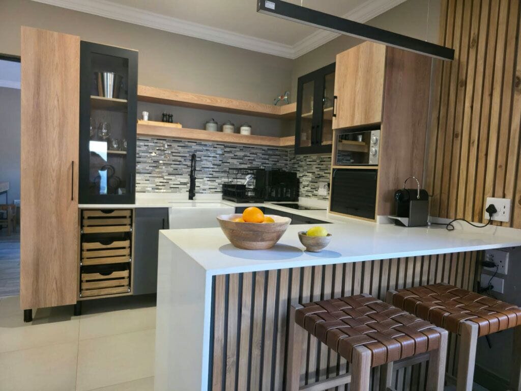 Eine moderne Küche mit Holzschränken, einer zentralen Kochinsel mit Hockern und einer Rückwand aus Stein.