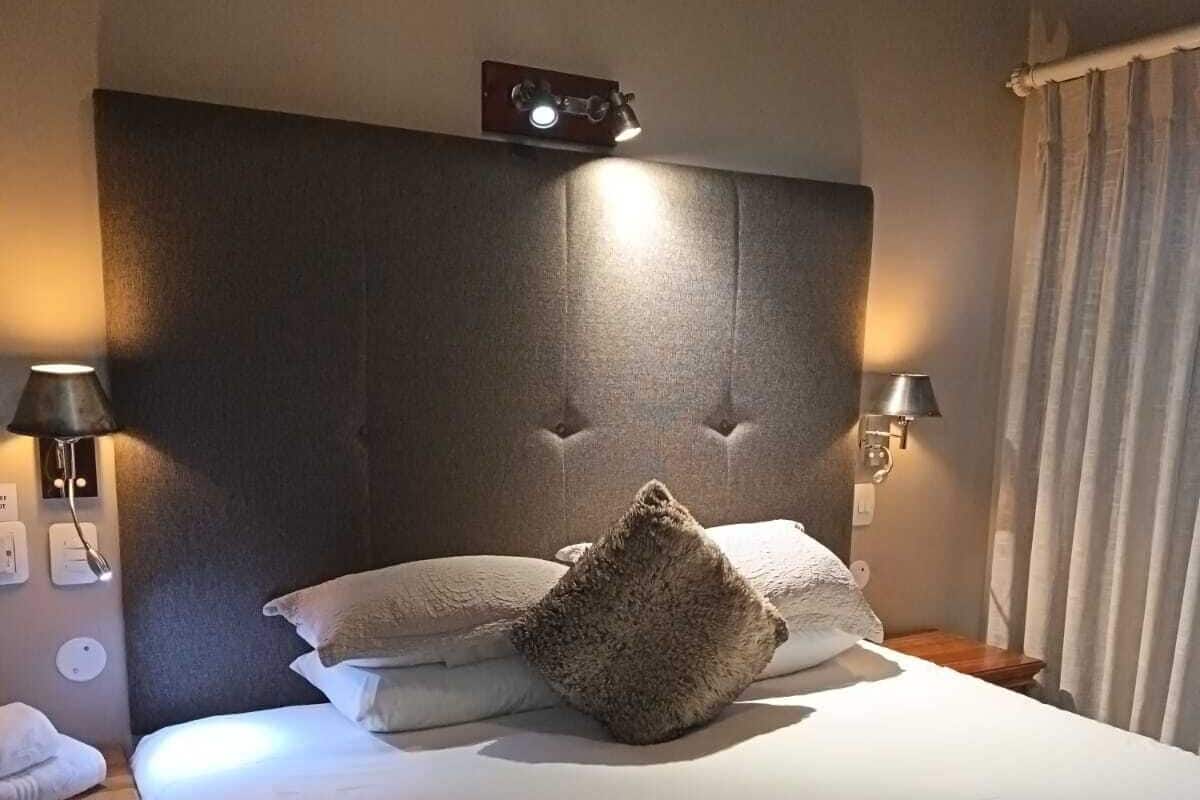 A neatly made bed with a large pillow, two bedside lamps, and a clock on the headboard.