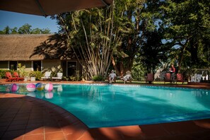 A swimming pool with lounge chairs and a thatched-roof building in the background. - Fairview Hotels, Spa and Golf Resort (Tzaneen)