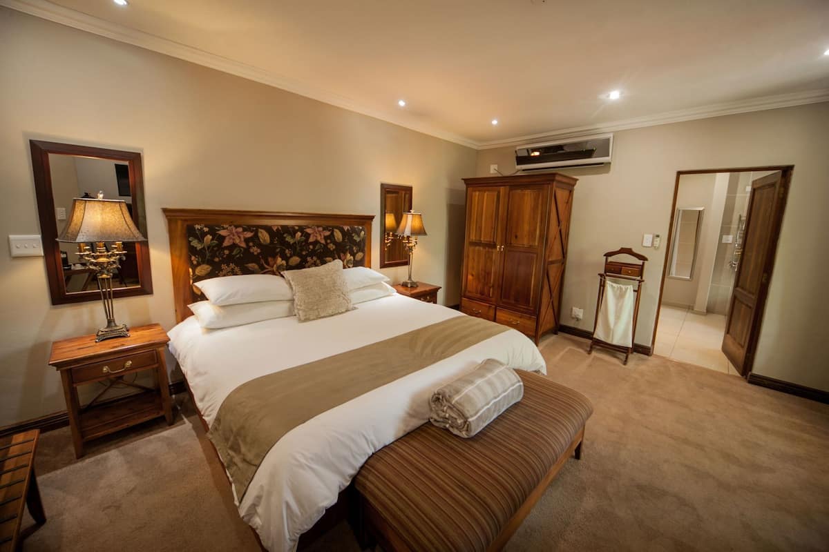 A hotel room with a large bed, two bedside tables, a wardrobe, an air conditioning unit, a mirror, and a bathroom with a shower and toilet.