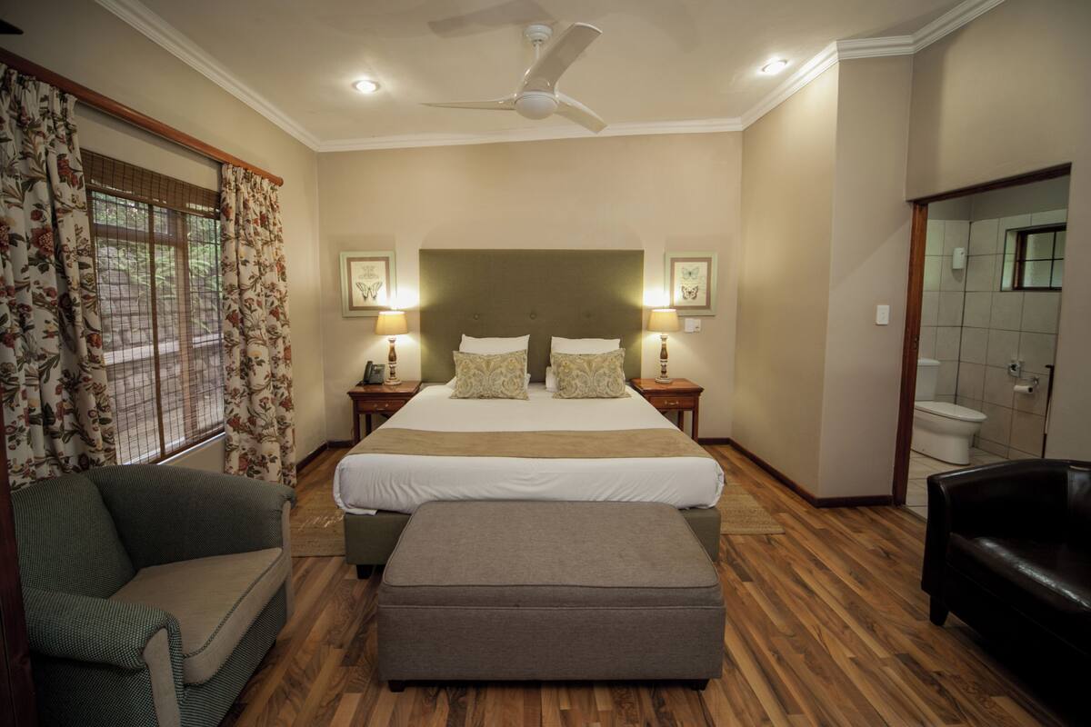 A bedroom with a large bed, two bedside tables with lamps, a ceiling fan, a sofa, and a wooden floor.