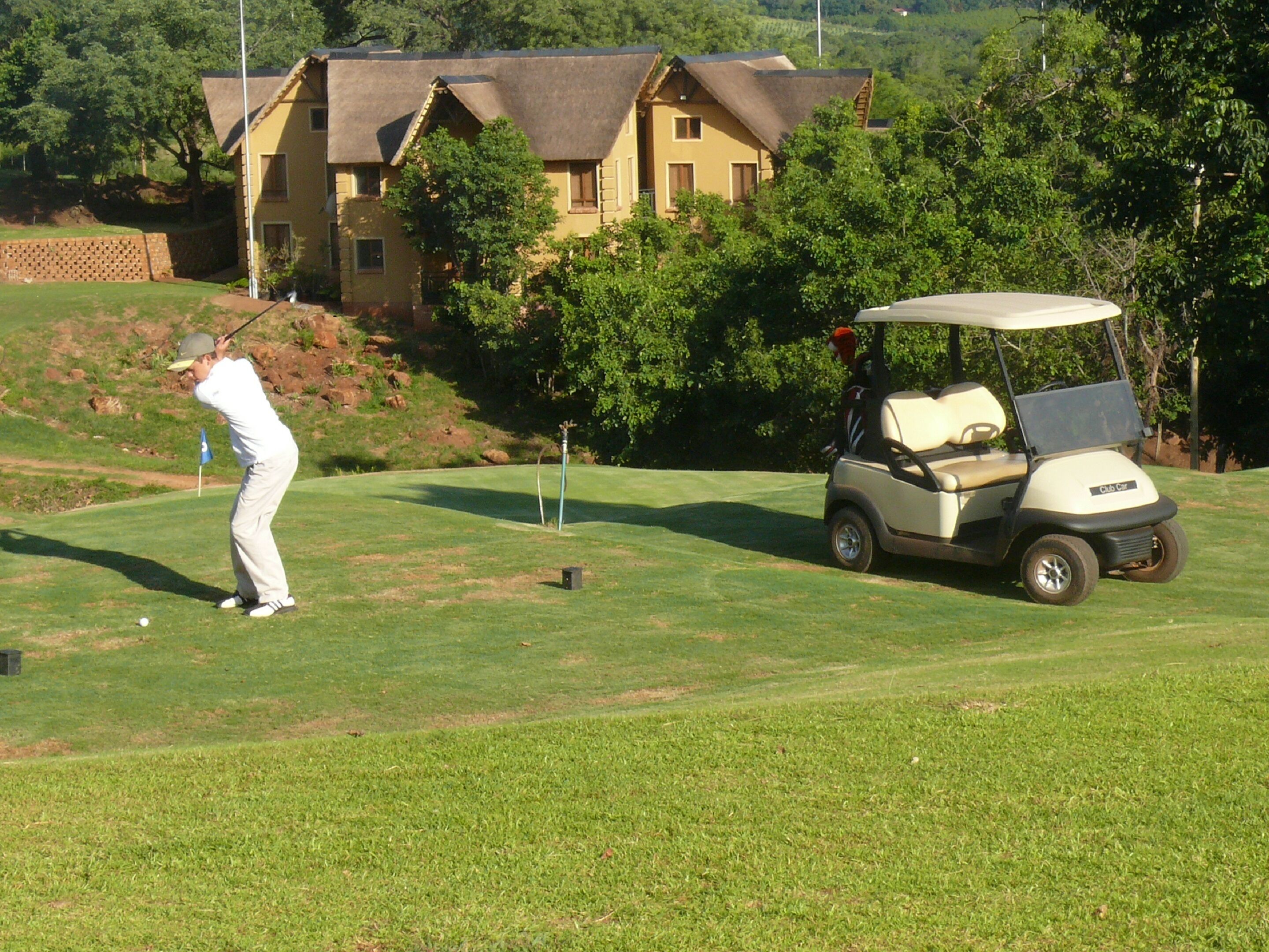 A golf course with a golf cart and a golfer in action.