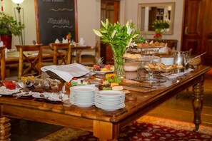 A buffet table with various food items, plates, and a vase of flowers. - Fairview Hotels, Spa and Golf Resort (Tzaneen)