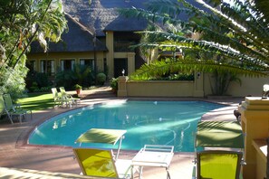 A pool area with lounge chairs and a thatched-roof building. - Fairview Hotels, Spa and Golf Resort (Tzaneen)
