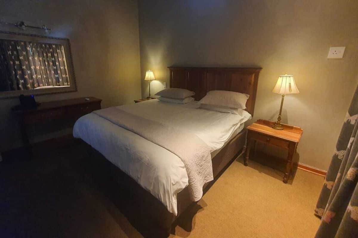 A bedroom with a large bed, two bedside tables with lamps, a nightstand, and a wall-mounted lamp.