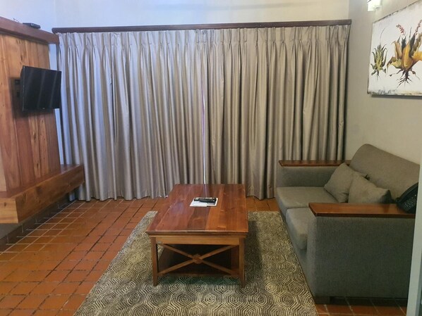 A living room with a wooden coffee table, a grey sofa, and a patterned rug. - Fairview Hotels, Spa and Golf Resort (Tzaneen)