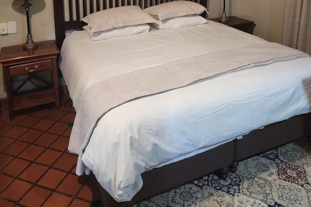 A neatly made bed with a wooden headboard, two bedside tables with lamps, and a patterned rug on a tiled floor.
