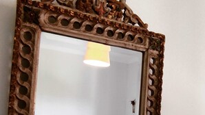 A mirror with an ornate frame reflecting a bed with white bedding and a small stool. - Flower House 🏡🌻 (Santo Tirso)