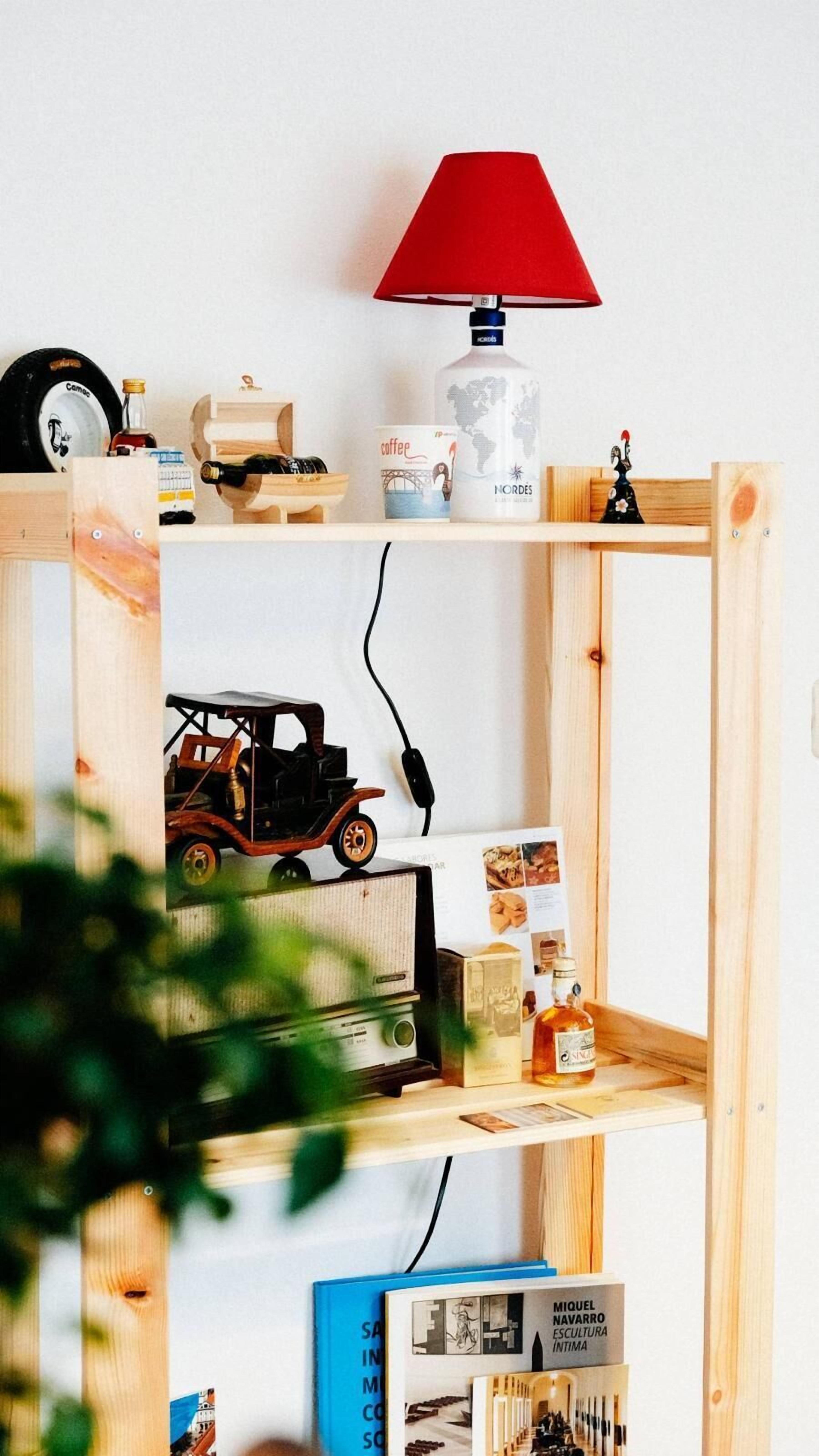Een houten plank met diverse objecten, waaronder een rode lamp, een fles, een koffiekop en een vintage radio.