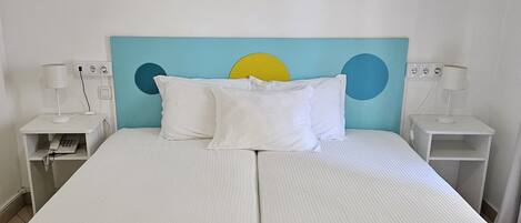 Una cama doble con cabecera azul, ropa de cama blanca y un cuadro colgado en la pared de una rosa.