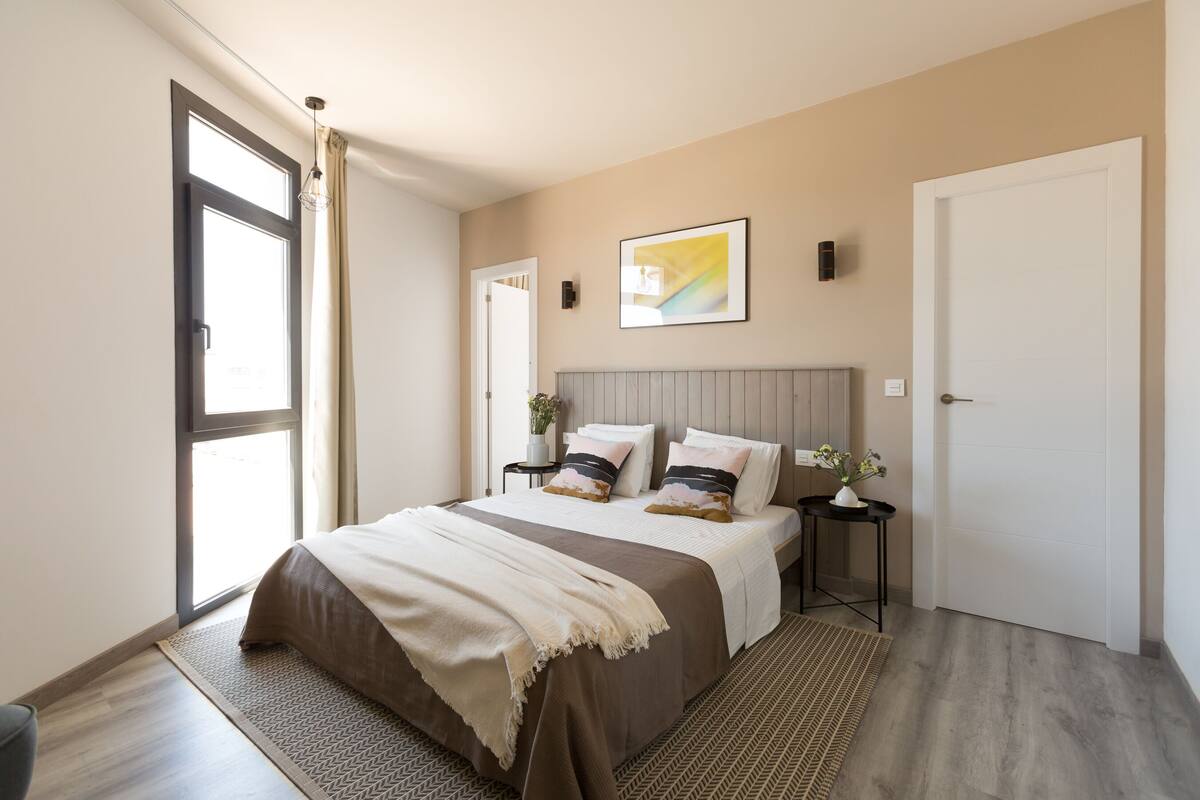 Une chambre moderne avec un grand lit, des tables de chevet, une œuvre d’art accrochée au mur et une porte.