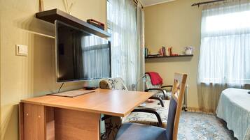 A compact hotel room with a wooden desk, a television, a chair, and a bed with a patterned bedspread.