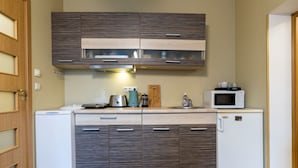 A compact kitchen with wooden cabinets, a built-in microwave, a kettle, and a small refrigerator. - Quiet romantic place Tartu Home Apts. (Tartu)