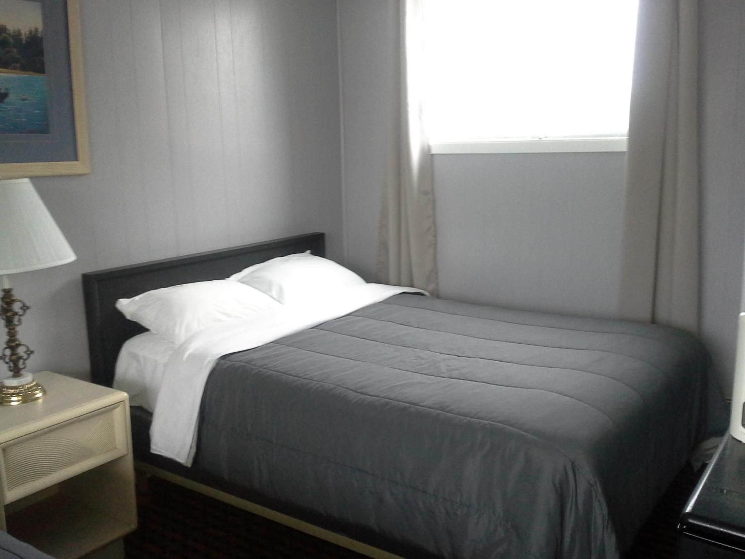 A neatly made bed with a grey bedspread and white pillows in a hotel room.