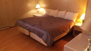 Un lit bien fait, recouvert d’une couverture marron, avec deux lampes de chevet et un plancher en bois.