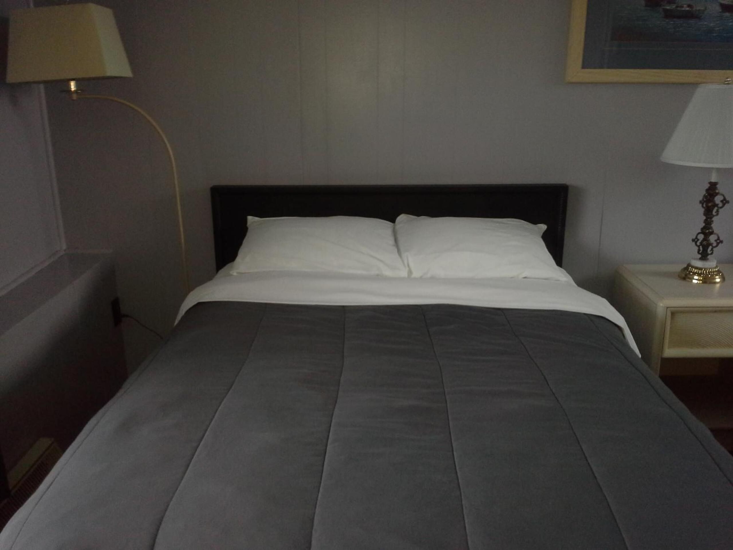 Een netjes opgemaakt bed met een donkergrijze deken en witte kussens in een hotelkamer.