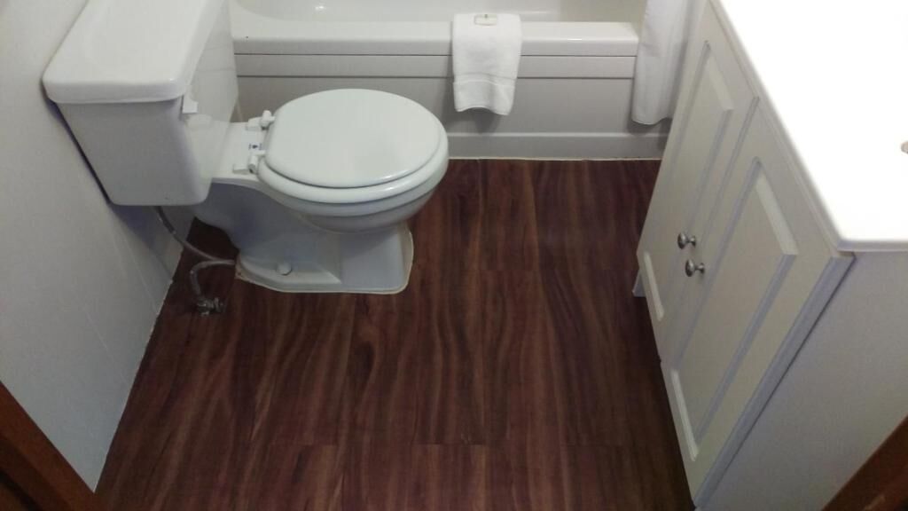 A small bathroom with a white toilet, a bathtub, and a wooden floor.