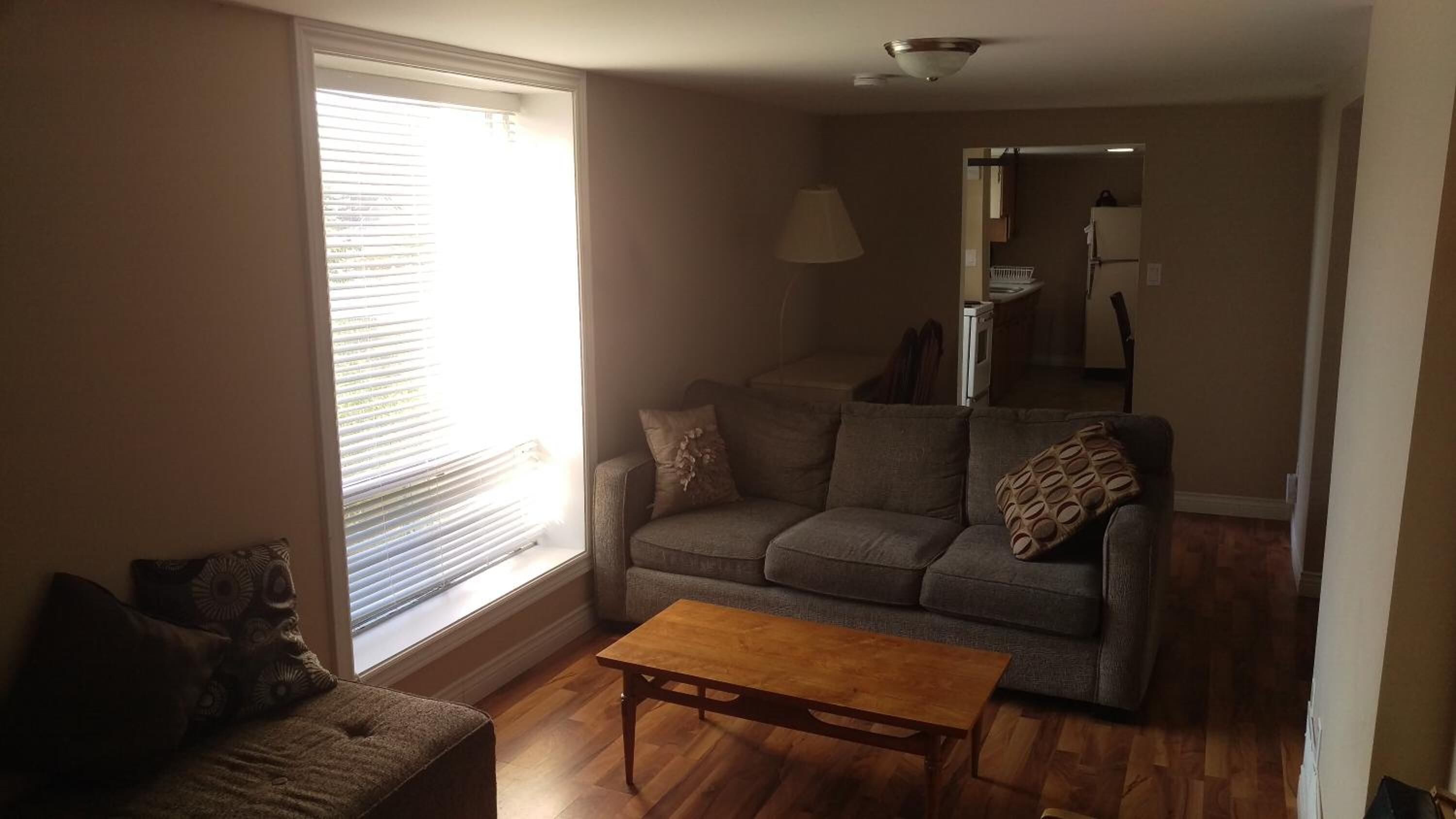 A living room with a sofa, a coffee table, and a window with blinds.