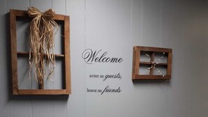 Un mur orné de deux cadres en bois, l’un représentant une vigne et l’autre une petite plante. En dessous, une pancarte indique : « Bienvenue, entrez en tant qu’invités, repartez en tant qu’amis. »