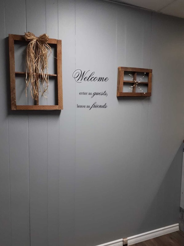 A wall with two wooden frames, one with a vine and the other with a small plant. Below, a welcome sign reads "Welcome enter as guests, leave as friends." - Bay Lake Inn (Frontiersman Motel) (Latchford)