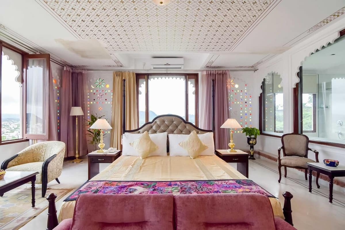 A spacious bedroom with a large bed, two nightstands, a chair, and a view of the city.