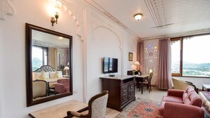 Une chambre d’hôtel dotée d’un grand miroir, d’une télévision, d’un bureau, d’un canapé et offrant une vue sur les montagnes par la fenêtre.
