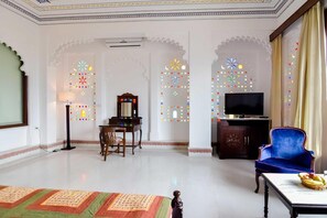 A room with a flat-screen TV, a blue armchair, a wooden cabinet, and a patterned rug. - Raj Kuber - A Boutique Lake View Hotel (Udaipur)