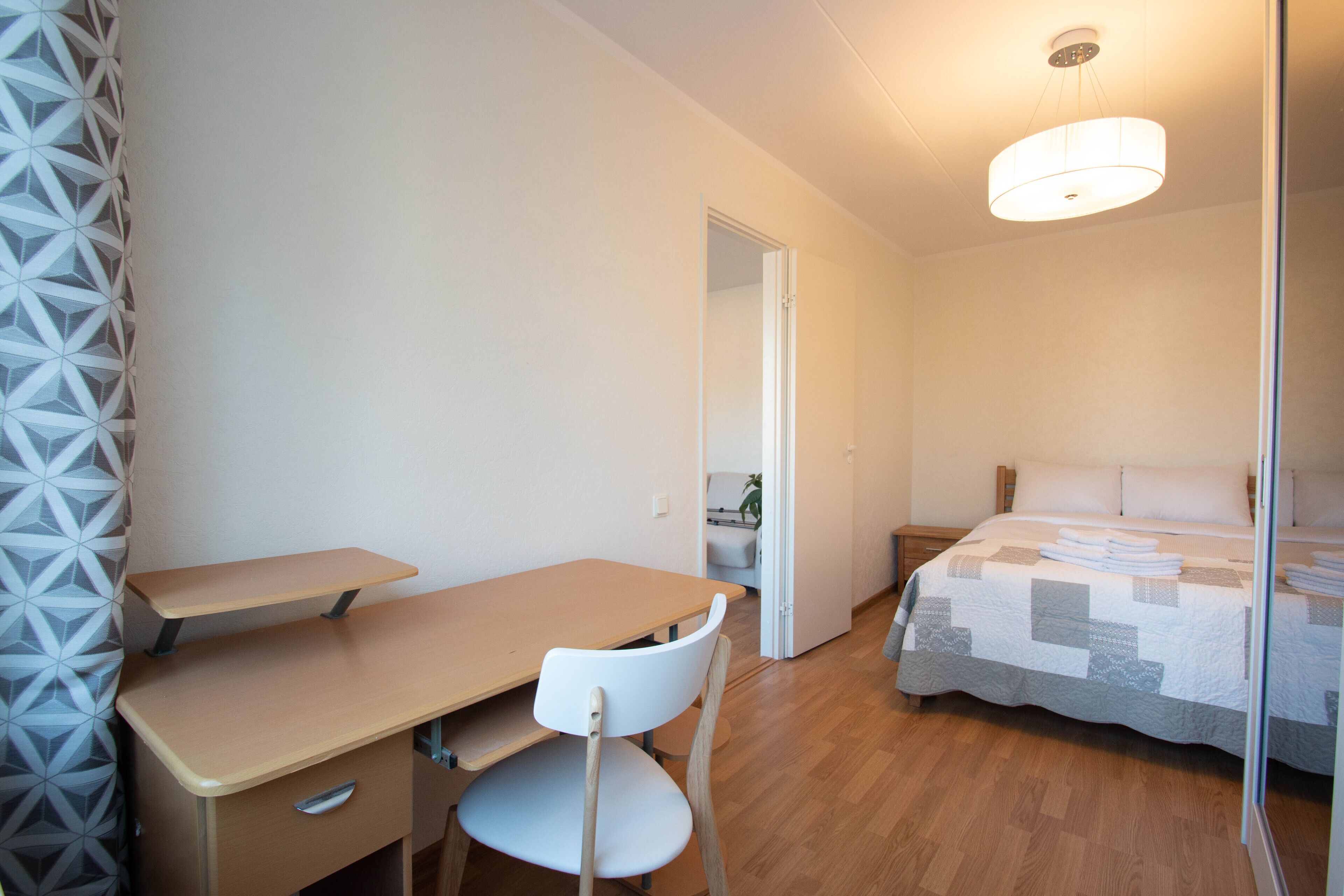 A bedroom with a bed, a desk, and a chair. There is a door leading to another room.