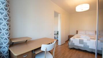 A bedroom with a bed, a desk, and a chair. There is a door leading to another room.