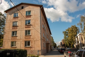 Un edificio de varios pisos con fachada plana, varias ventanas y un contenedor de basura visible.