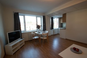 Una sala de estar moderna con televisor de pantalla plana, mesa de comedor, sillas y una pequeña área de cocina con armarios y un radiador.