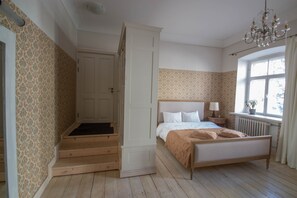 A bedroom with a bed, a nightstand, a window with curtains, a radiator, and a staircase leading to an upper room. - Old Town Library Deluxe Tartu Home Apt. (Tartu)