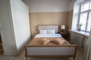 A bedroom with a large bed, a nightstand, a potted plant, and a window with a view. - Old Town Library Deluxe Tartu Home Apt. (Tartu)