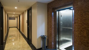 A hotel corridor with a marble floor, a trash bin, and an elevator.